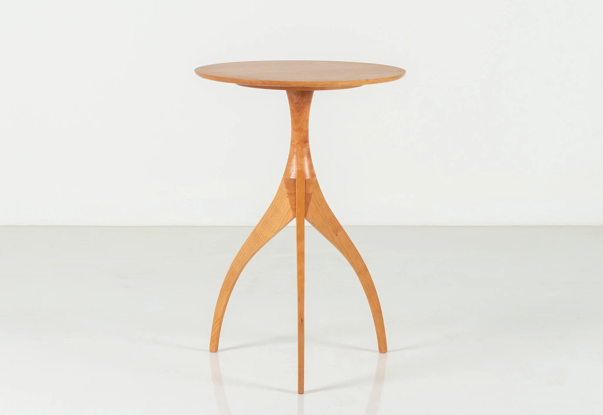 Table - Made of solid, hand-finished hardwood, the table features three legs that arc as they rise, forming a reverse
